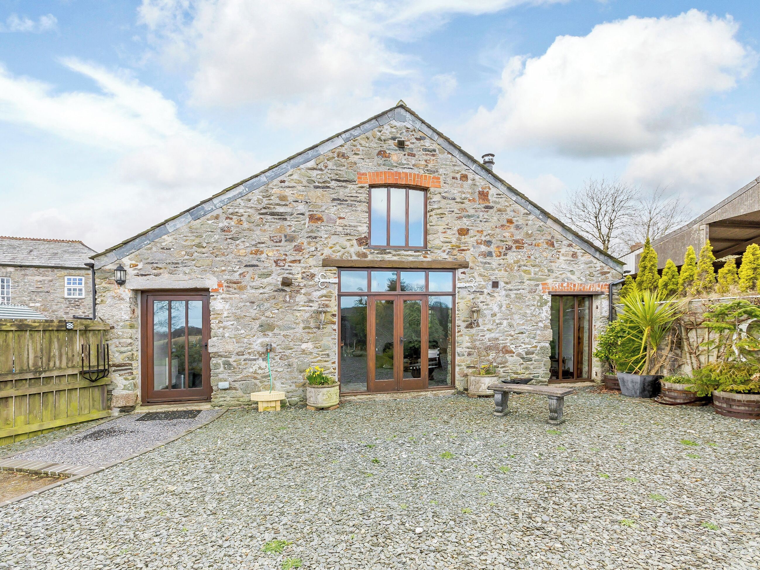 A stone building with a sloped roof, wooden doors, and a gravel driveway.