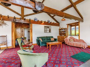 Un intérieur rustique avec des poutres apparentes, un canapé vert, une moquette à motifs et un meuble traditionnel.