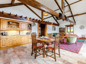 Une cuisine rustique avec des poutres en bois, une table à manger avec des chaises et un coin salon avec un canapé et un fauteuil.