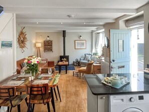 A cozy living room with a fireplace, a dining area with wooden furniture, and a kitchen with a washing machine. - 2 bedroom accommodation in Kingsand (Kingsand)