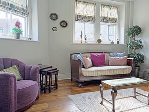 A cozy living room with a purple armchair, a sofa with multiple cushions, a wooden coffee table, and a large window with decorative window treatments. - 2 bedroom accommodation in Helmsley (Helmsley)