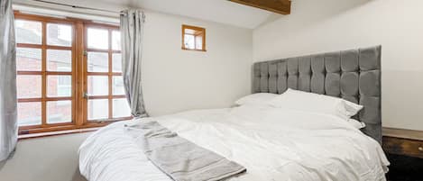 A bedroom with a bed, a window with curtains, a small picture frame, and exposed wooden beams.
