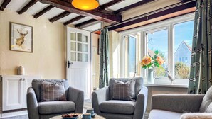 Un salon chaleureux avec deux fauteuils gris, une petite table basse ronde et une fenêtre donnant sur une maison et de la verdure.