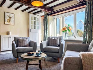 Un salón acogedor con dos sillones grises, una mesita redonda y un ventanal con vistas a una casa y follaje.
