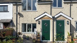 A two-story house with a green door, a satellite dish, and a garden with potted plants.