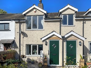 A two-story house with a green door, a satellite dish, and a garden with potted plants.