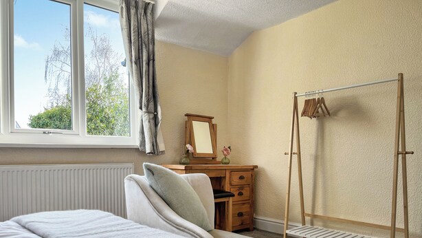 Une chambre à coucher avec un lit, une commode, un miroir, un radiateur et une fenêtre avec des rideaux.