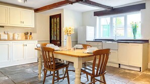 Une cuisine avec des meubles blancs, une table à manger en bois et deux chaises.