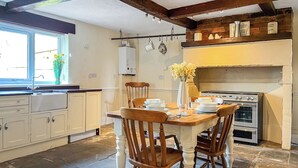 A kitchen with wooden chairs, a dining table set for four, a stove, and a window with flowers.