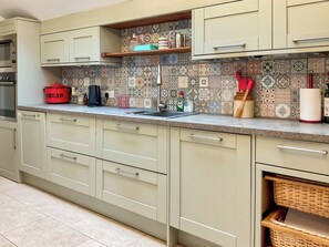 A kitchen with light green cabinets, a tiled backsplash, a red pot labeled 'BREAD,' a coffee maker, and various kitchen utensils. - 1 bedroom accommodation in Ashmore, near Shaftesbury, (Ashmore, near Shaftesbury,)