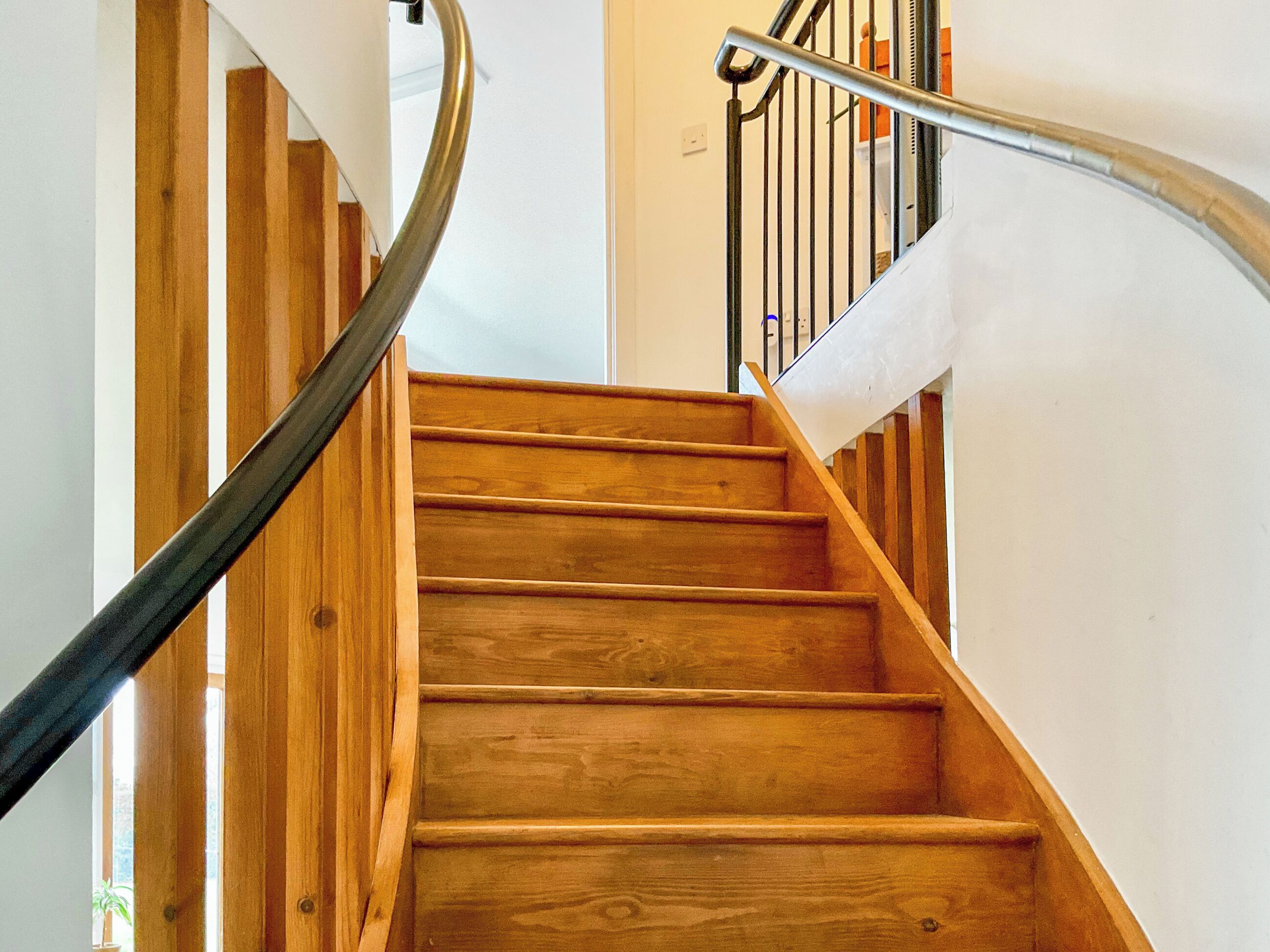 Una escalera de madera con barandilla de metal, paredes blancas y suelo de madera.