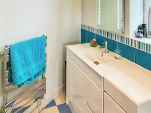 Un bany amb un lavabo blanc, un mirall, una barra de tovalloles i un sòl emblumat.