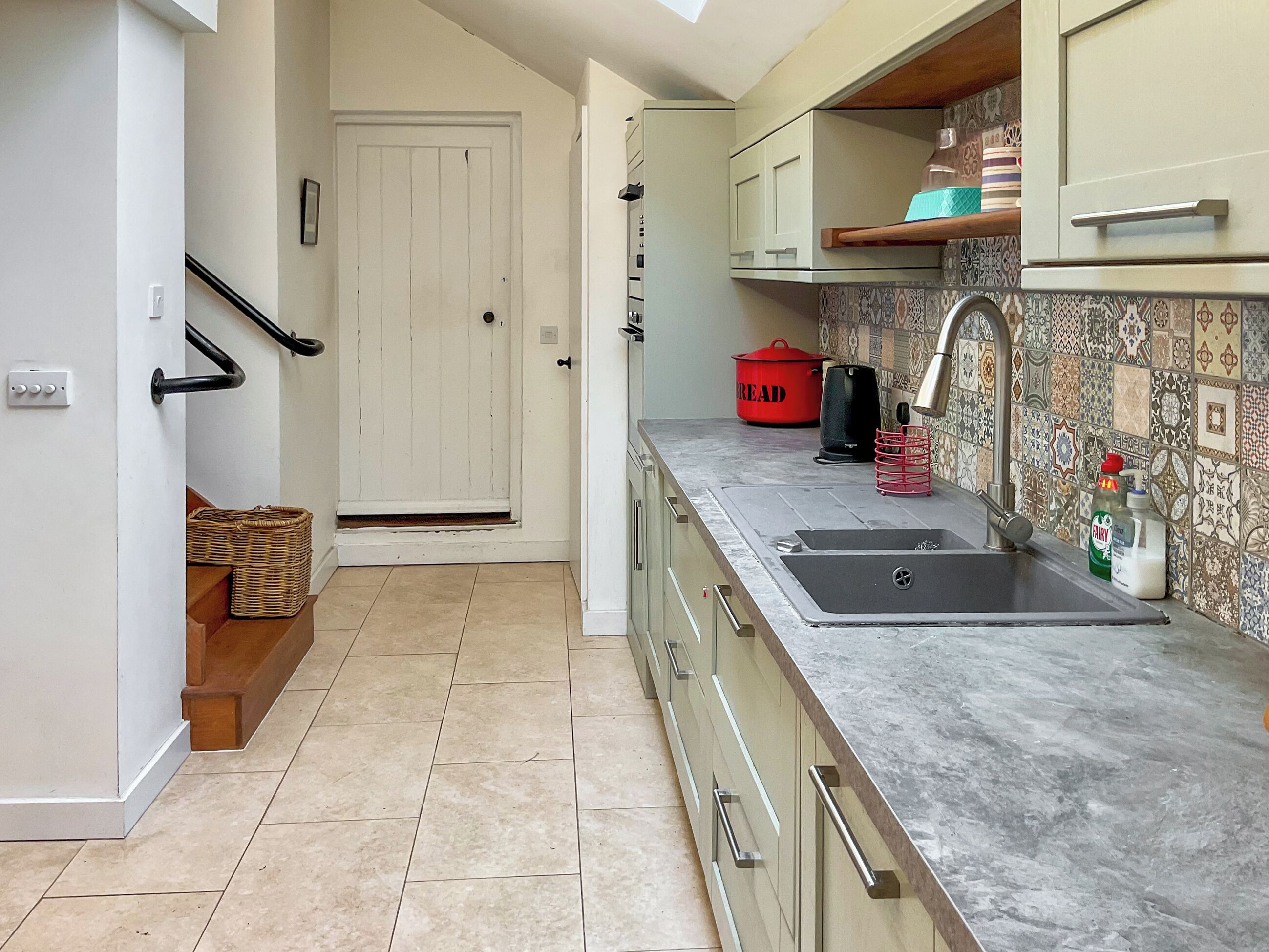 A kitchen with a sink, a red pot, and a bottle of Fairy dish soap.