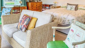 Et hyggeligt værelse med sofa, seng med blomstret sengetøj, en trækommode og et vindue med gardiner.