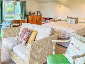 A cozy room with a sofa, a bed with floral bedding, a wooden dresser, and a window with curtains.