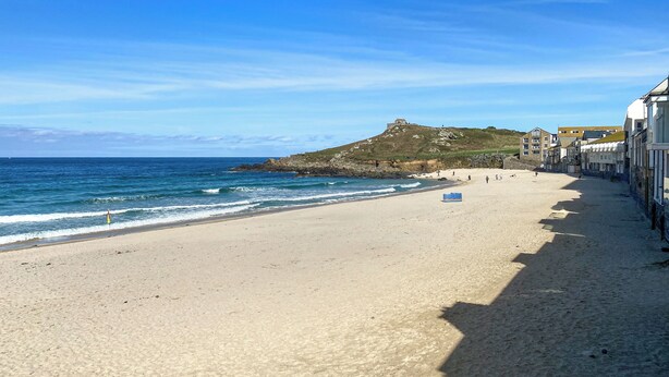Una playa con cielo despejado, orilla arenosa y edificios a lo largo de la costa.