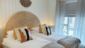 Una cama doble con cabecera de madera, dos mesitas de noche y una ventana con cortinas.