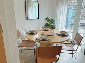 A dining area with a round table set for four, surrounded by chairs, with a potted plant and a window in the background. - 2 bedroom accommodation in Hayle (Hayle)