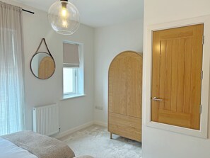 Ein Schlafzimmer mit einem Bett, einem Holzschrank, einem Spiegel, einem Fenster und einer Heizung.