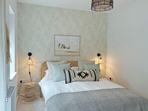 A bedroom with a bed, two wall-mounted lamps, a round wooden stool, a radiator, and a framed picture on the wall. - 2 bedroom accommodation in Hayle (Hayle)
