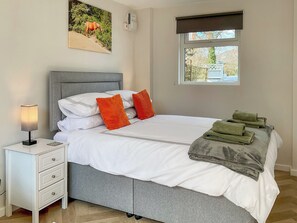 A neatly made bed with pillows, a bedside lamp, a nightstand with drawers, and a window with a view of the outside. - 1 bedroom accommodation in New Milton, near Bournemouth (New Milton, near Bournemouth)