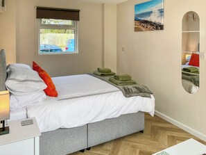 A neatly made bed with pillows and a blanket, a bedside table with a lamp and a decorative item, a window with a view of the outside, and a painting on the wall. - 1 bedroom accommodation in New Milton, near Bournemouth (New Milton, near Bournemouth)