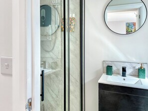 A bathroom with a glass shower enclosure, a white sink with a marble countertop, and a round mirror on the wall. - 1 bedroom accommodation in New Milton, near Bournemouth (New Milton, near Bournemouth)