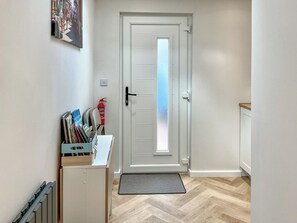 A hallway with a white door, a radiator, a fire extinguisher, a mat, and a shelf with books and a guest book. - 1 bedroom accommodation in New Milton, near Bournemouth (New Milton, near Bournemouth)
