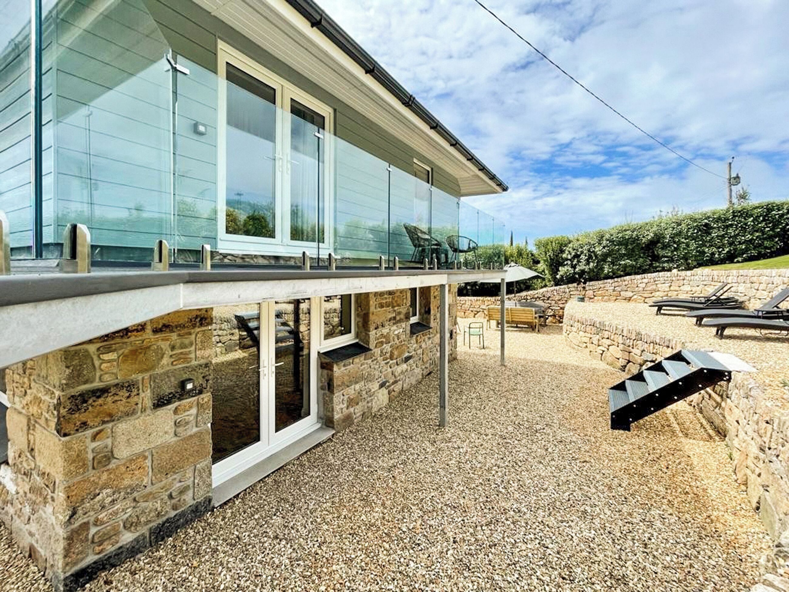 A modern house with a stone foundation, large windows, and a patio area with outdoor furniture.