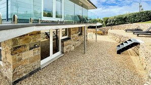 A modern house with a stone foundation, large windows, and a patio area with outdoor furniture. - 4 bedroom accommodation in St Just (St Just)