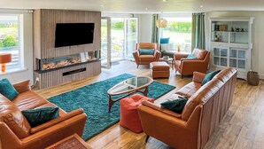 A living room with a fireplace, leather sofas, a coffee table, and a television. - 4 bedroom accommodation in St Just (St Just)