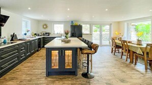 A spacious kitchen with a large island, dark cabinetry, and a dining area with wooden furniture. - 4 bedroom accommodation in St Just (St Just)