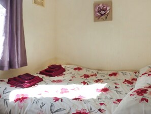 A room with a bed, a window with curtains, and a wall-mounted artwork.