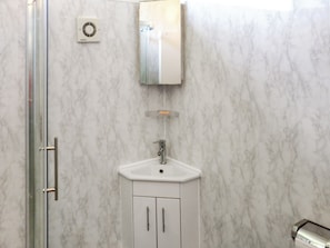 Une salle de bain avec une douche à parois de verre, un lavabo blanc avec un miroir au-dessus, et des murs en marbre.