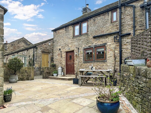 A stone building with a wooden door, windows, and a bench in the courtyard. - 3 bedroom accommodation in Chisworth (Chisworth)