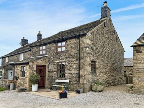 A stone building with a wooden door, windows, and a bench outside. - 3 bedroom accommodation in Chisworth (Chisworth)