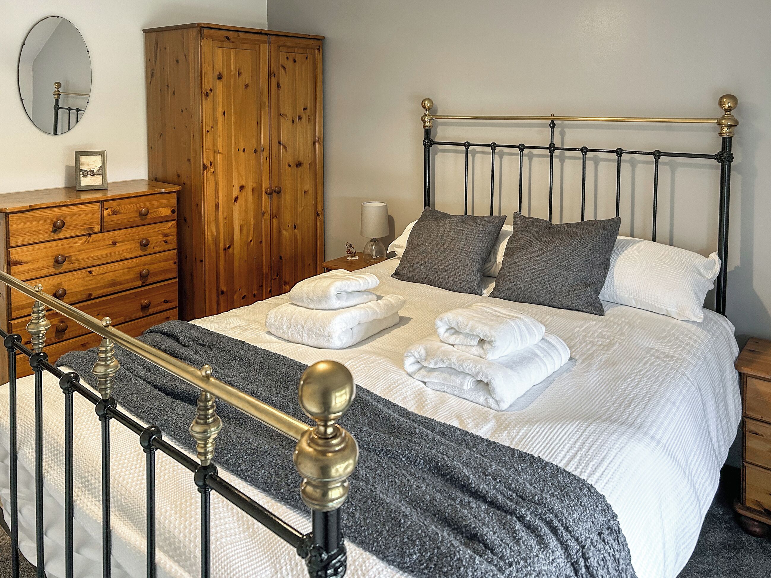 A neatly made bed with white linens and towels, a wooden wardrobe, a mirror, and a metal-framed headboard.