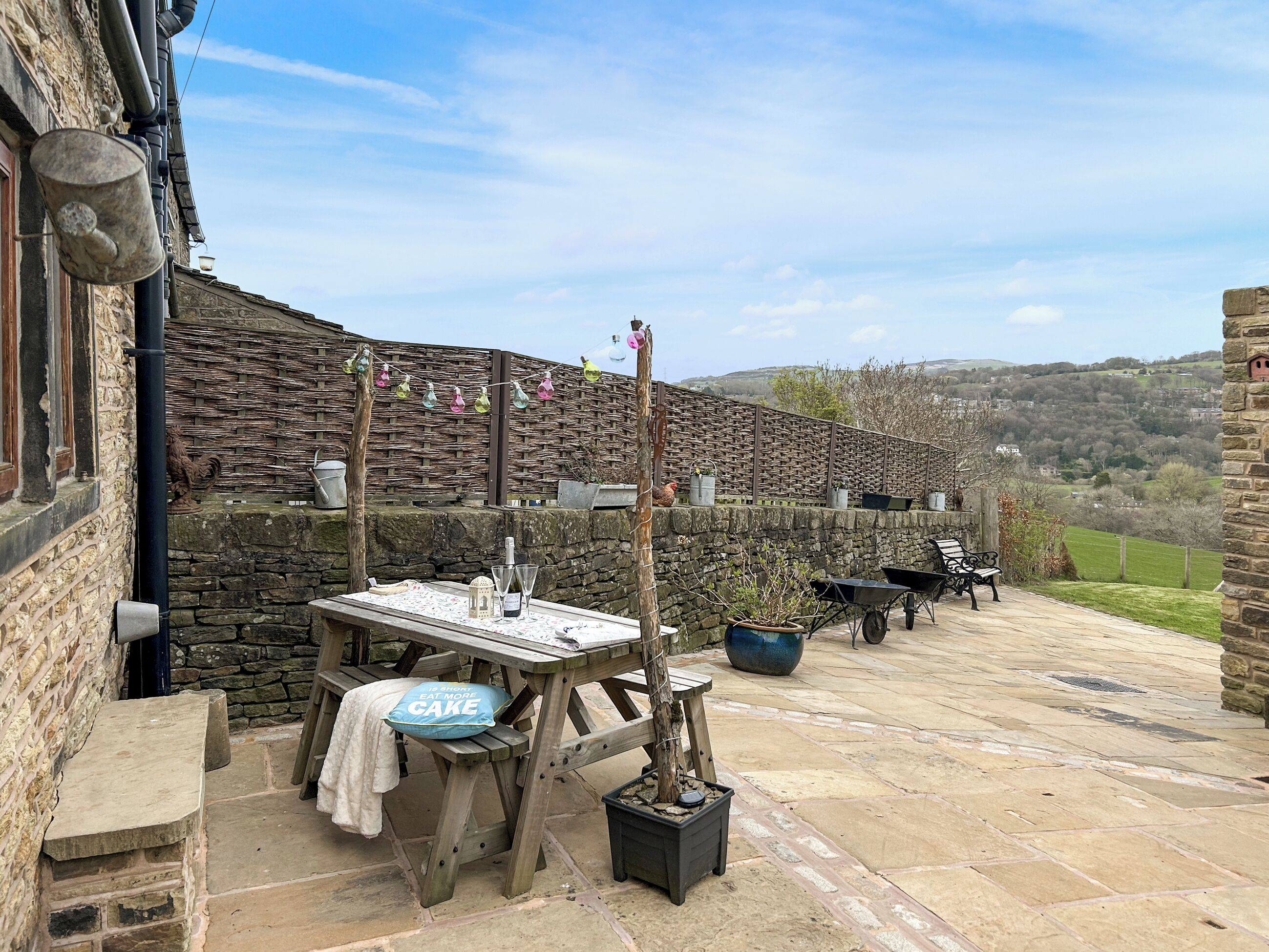 A rustic outdoor seating area with stone walls, a wooden table, and a view of the countryside.