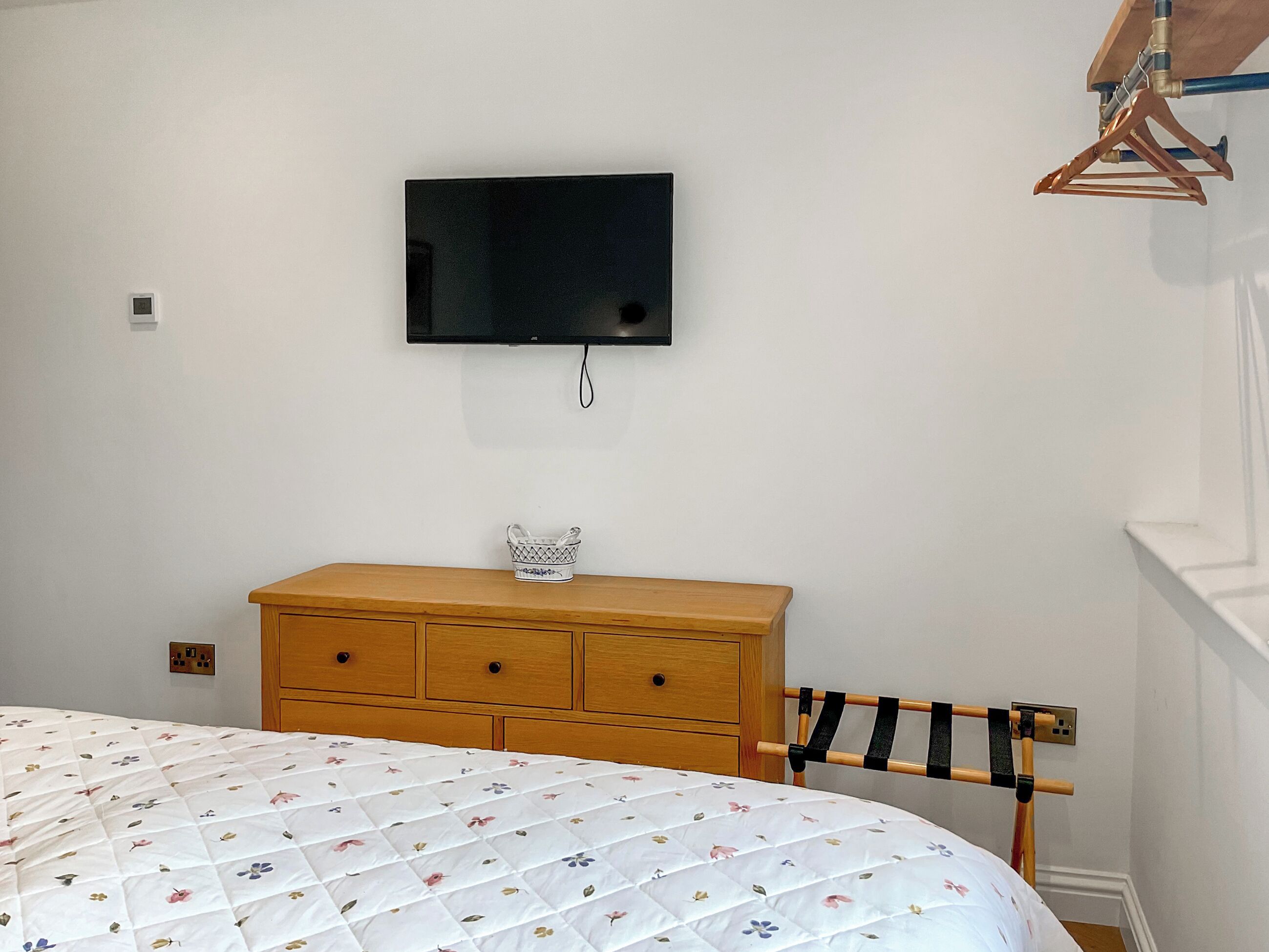 A bedroom with a bed, wooden dresser, and a mounted television.