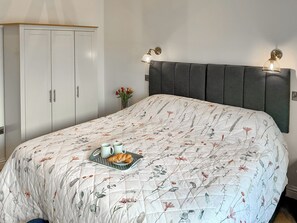 Ein Schlafzimmer mit einem Bett, einem Kleiderschrank, einem Nachttisch mit Blumenvase und Wandleuchten.