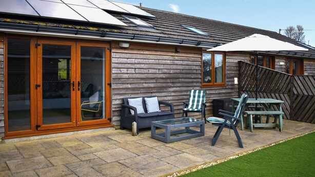 A wooden cabin with a patio area, including a sofa, chairs, and a table. - 1 bedroom accommodation in Tytherleigh, near Axminster (Tytherleigh, near Axminster)