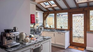 A kitchen with a stone wall, wooden beams, a fire blanket, a coffee machine, and a stove. - West House - UK51668 (Leyburn)