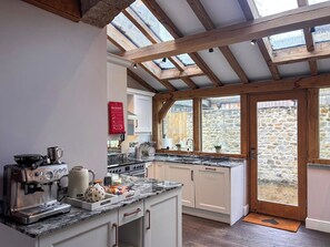 A kitchen with a stone wall, wooden beams, a fire blanket, a coffee machine, and a stove. - West House - UK51668 (Leyburn)