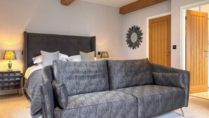 A bedroom with a bed, a grey sofa, a wooden door, and a wall-mounted mirror. - West House - UK51668 (Leyburn)