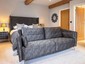 A bedroom with a bed, a grey sofa, a wooden door, and a wall-mounted mirror. - West House - UK51668 (Leyburn)