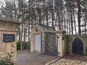 Een stenen poortgebouw met een metalen poort, een stenen muur en een bord waarop staat 'West House Private No Entry'.