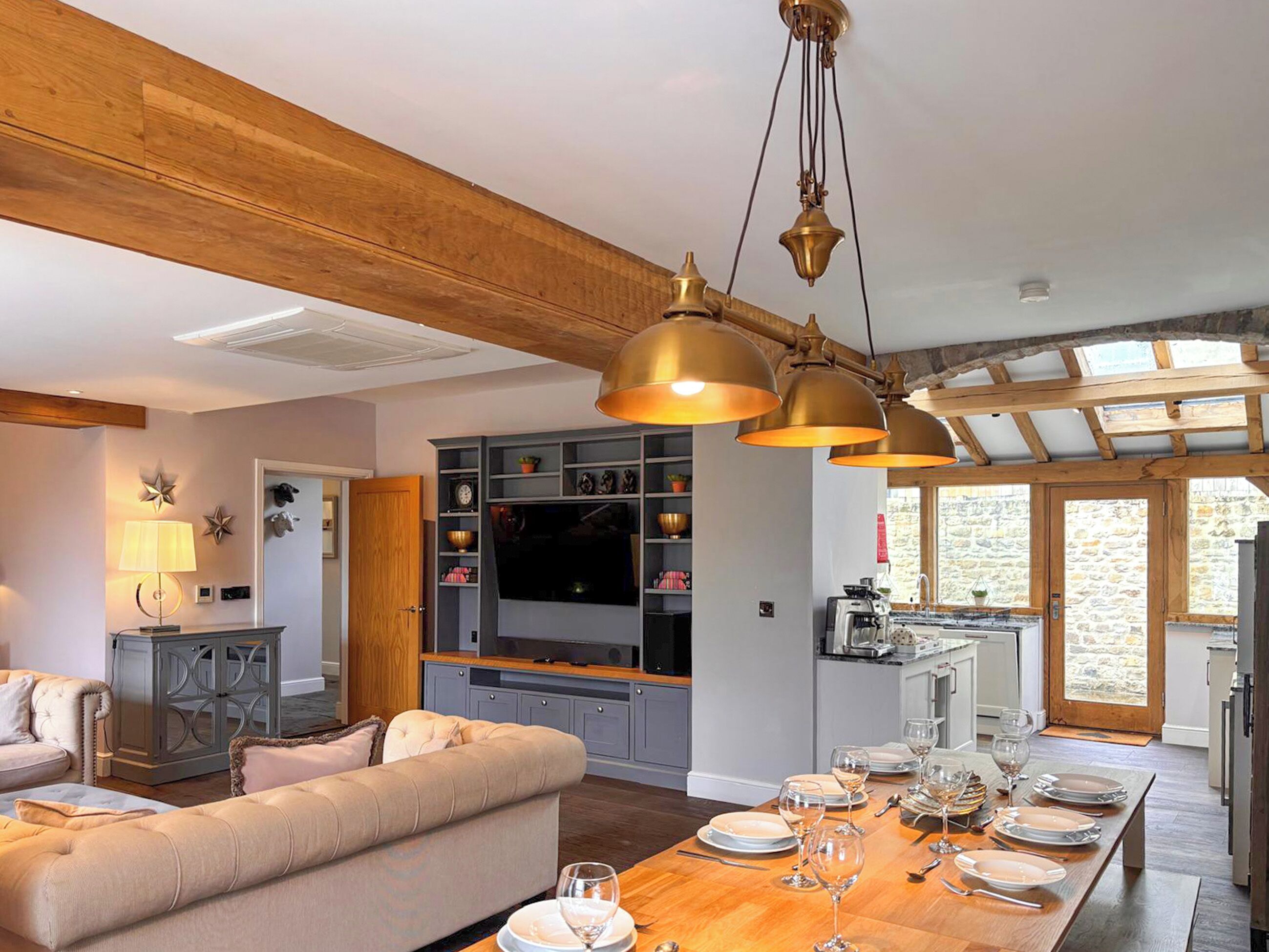 A modern kitchen with wooden beams, a dining area with a wooden table set for a meal, and a cozy living room with a sofa and decorative items.