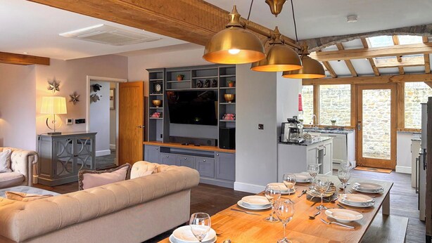 A modern kitchen with wooden beams, a dining area with a wooden table set for a meal, and a cozy living room with a sofa and decorative items. - West House - UK51668 (Leyburn)