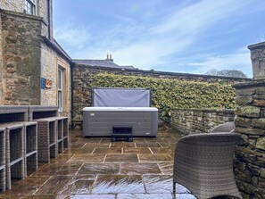 A stone building with a patio area featuring a large air conditioning unit, wicker furniture, and a stone wall with ivy. - West House - UK51668 (Leyburn)