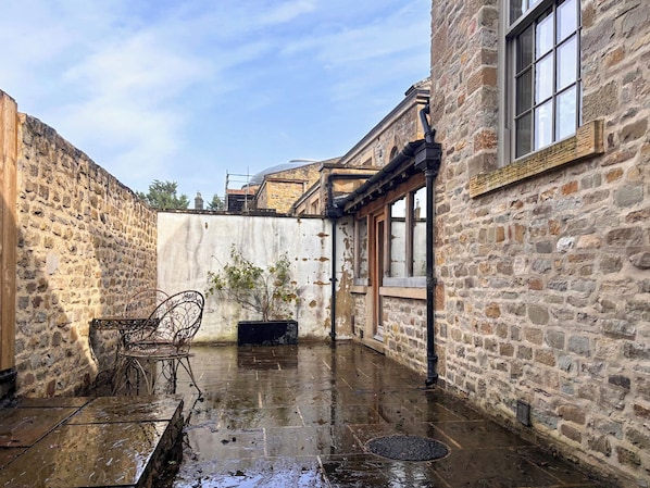 A stone courtyard with a metal chair, a potted plant, and a window.